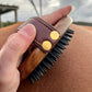 A side on view of the rubber brush in a person's hand. Showing the signiature beechwood material, black rubber bristles and gold detailing on the handle.