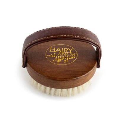 A view of the top side of the Hairy Pony Face Briush, showing the soft padded handle, gold logo detailing and beechwood material on the back of the brush.