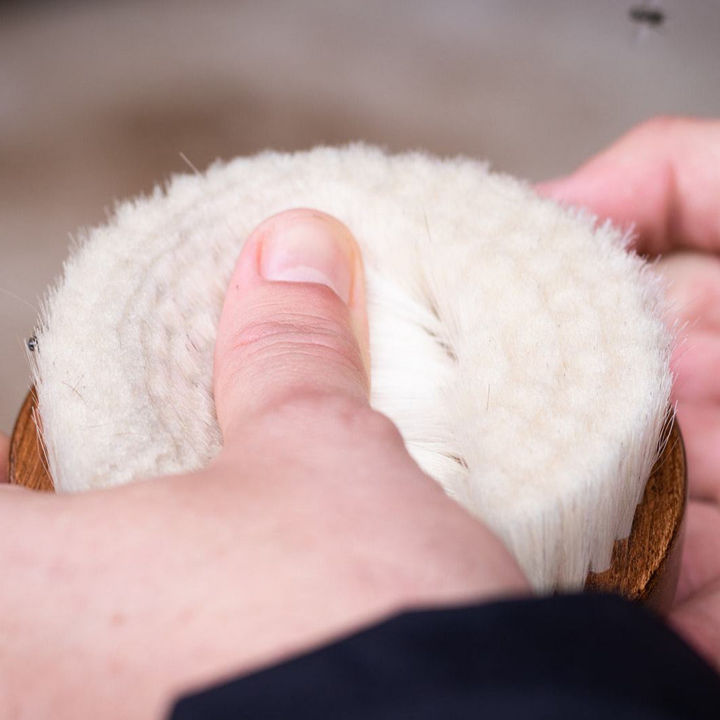 A close up of the Hairy Pony Face Brush, being held in a person's hand. Their thumb is bending back the bristles, showing how soft and flexible they are.